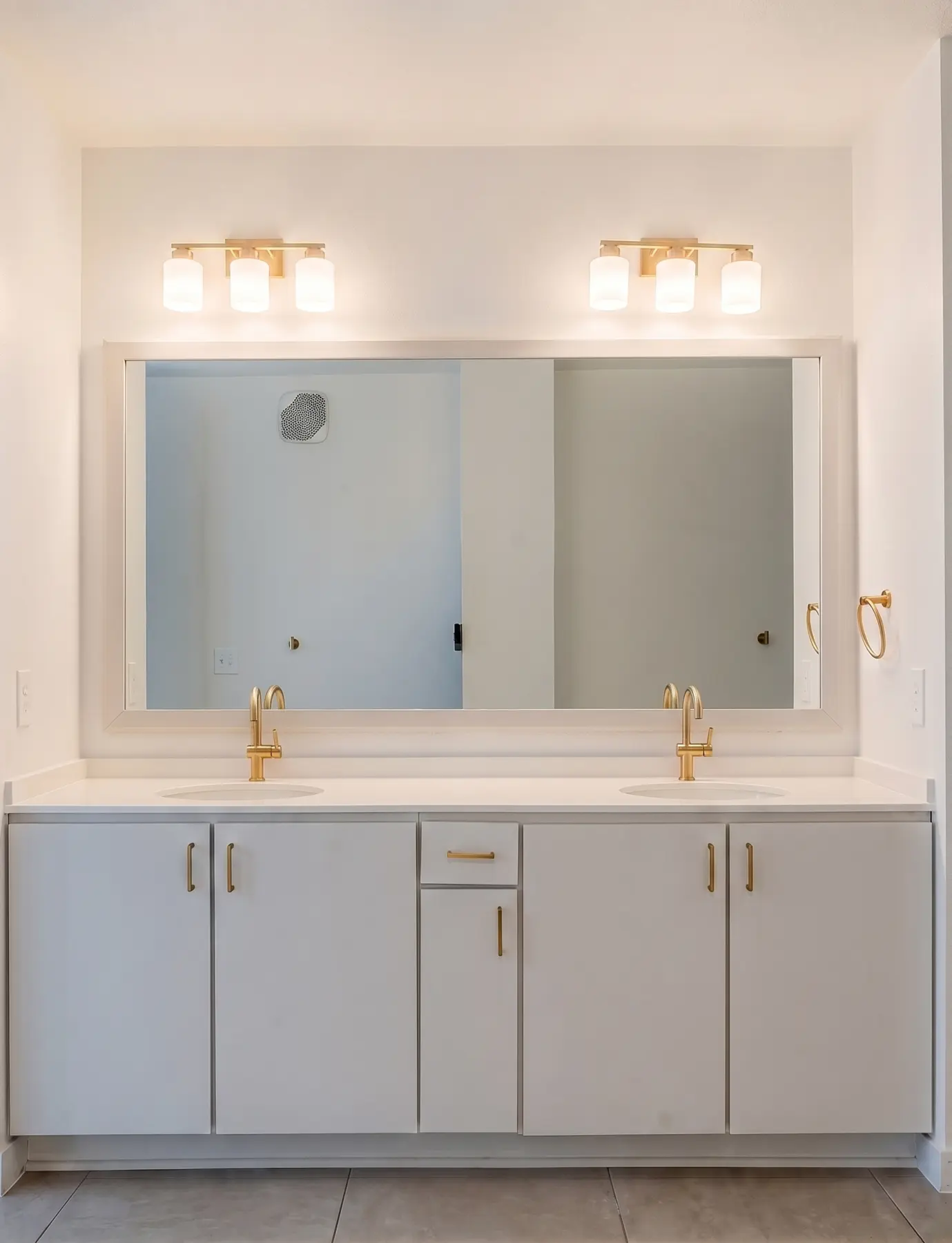 Renovated apartment bathroom with double vanity, new lighting, and brass fixtures